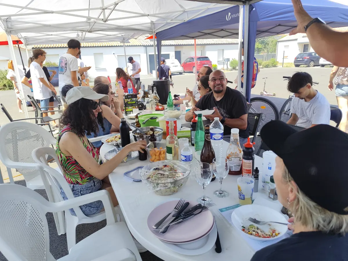 Voisins attablés partageant un repas sous les barnums, tout sourire.